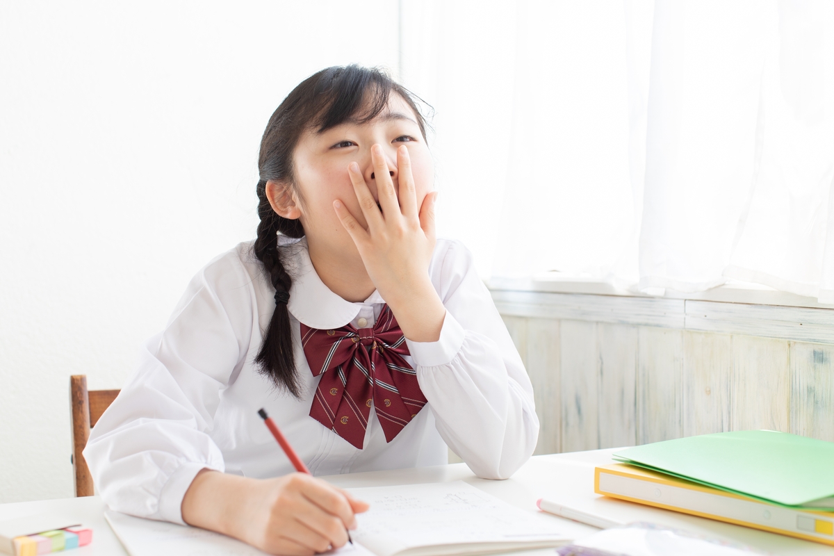 A sleepy young Asian student yawning while seated at a desk