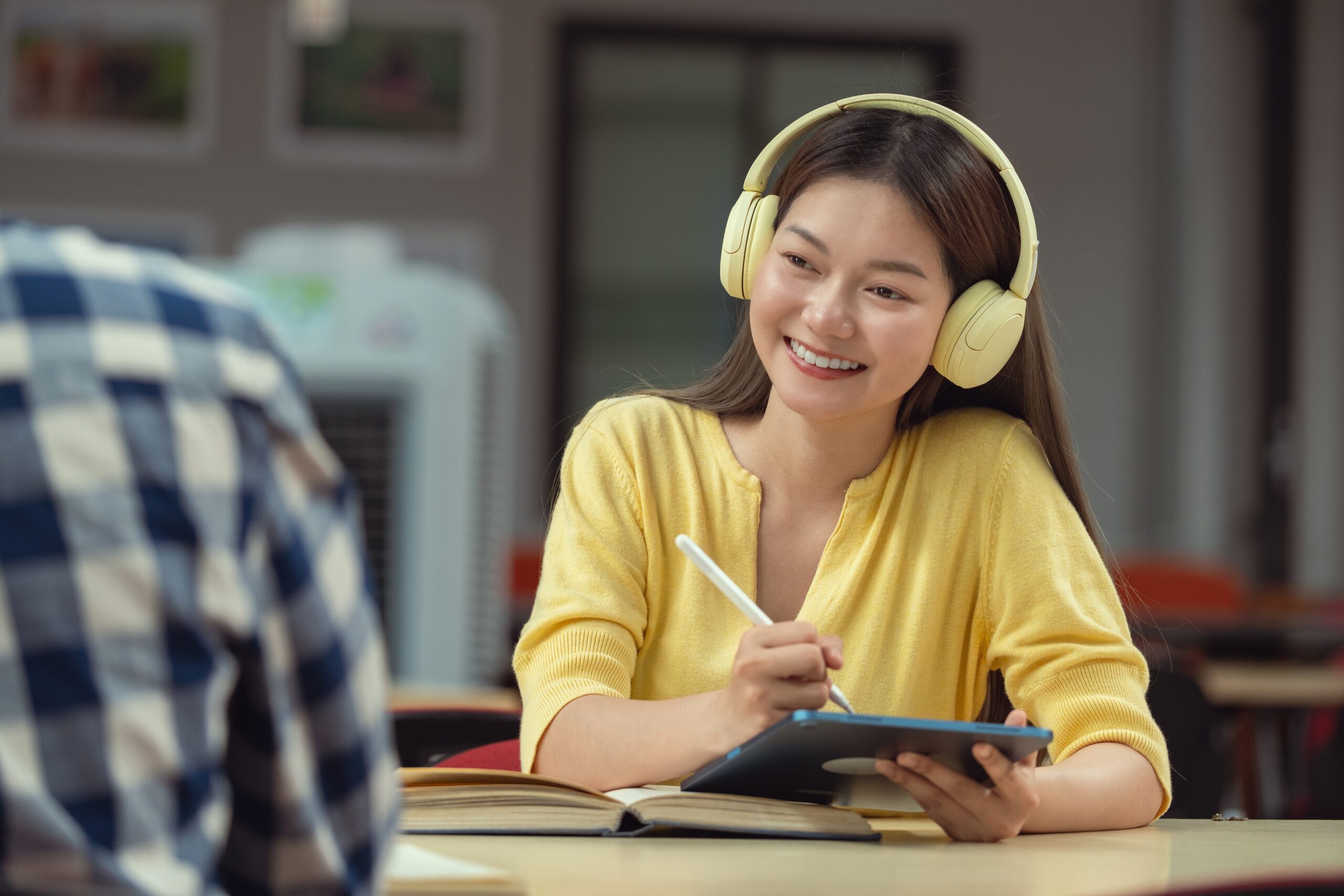 Young Asian woman smiling as she writes study notes at a desk